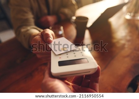 Hand tapping a credit card on a contactless card reader paying for coffee in coffee shop