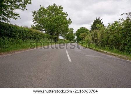 view along quiet country lane. Empty road with trees and hedges at the sides. Middle of a road. Road trip in rural England. Royalty-Free Stock Photo #2116963784
