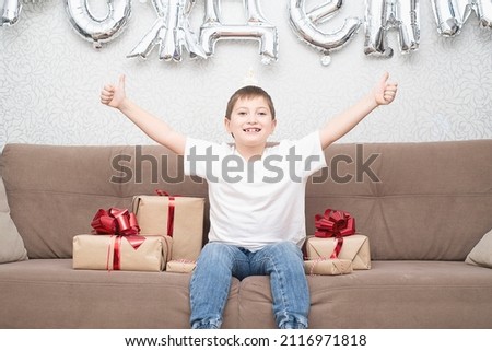 a boy is sitting on the sofa, smiling, raising his hands. He has his birthday and many gifts.