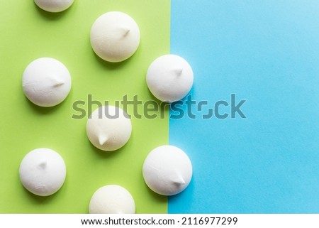 Pattern with delicate white meringue cookies. Meringues are lying in rows on blue green paper background. Unhealthy food concept. Minimal food concept. dessert design mockup, confectionery.