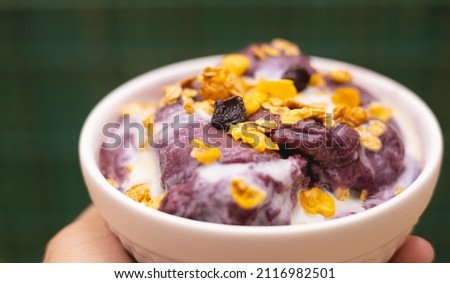 A person holding a açaí frozen in the bowl with granola and condensed milk. Close-up photo view and green background. Brazilian food.