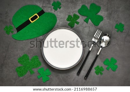 Happy St.Patriks day. Festive table setting for St.Patrick's day. Plate, cutlery, clover leaves and leprechaun hat on gray concrete table. Shamrock symbol of luck. Copy space, flat lay