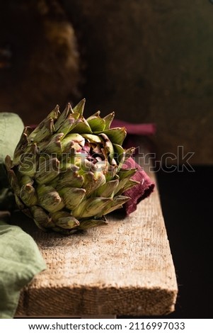 Fresh green artichoke on rustic wooden background with napkins, close up