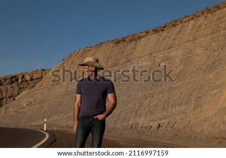 Adult man in cowboy on roadside on desert against mountain. Almeria, Spain
