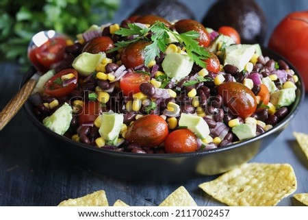 Homemade Mexican black bean and corn salad or Texas caviar bean dip lime dressing, Served with tortilla chips and fresh ingredients. Blurred background.