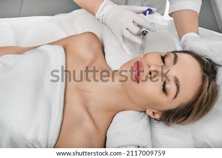 Female patient during lip augmentation procedure at beauty clinic with cosmetologist. Filler injection for beautiful female lips augmentation with hyaluronic Royalty-Free Stock Photo #2117009759