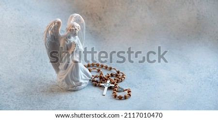 Praying angel figurine and rosary cross on abstract gray background. faith in God, Christianity church, pray, lent, religion concept. symbol of Christmas or Easter holiday. banner. copy space