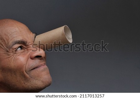 man looking through toy binoculars toilet paper roll on grey background stock photo