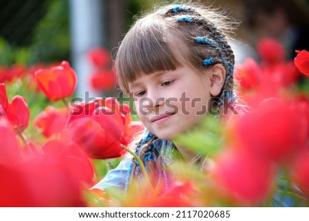 Happy child girl enjoying sweet smell of red tulip flowers in summer garden