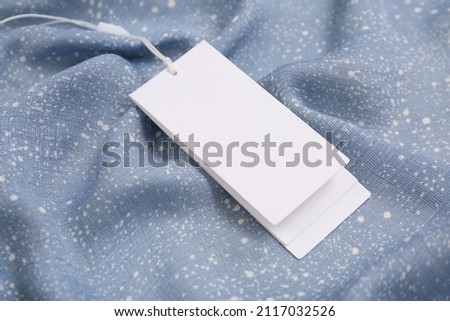 Blank white tags on light blue fabric, closeup. Space for text