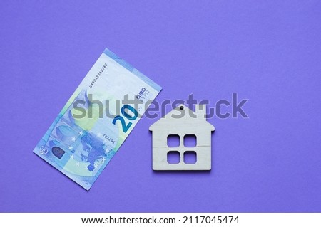 wooden small decorative house and paper money on purple background, copy space, sale and purchase of real estate concept. Real estate buying a house concept.