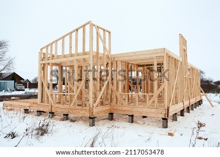 Wood frame house under construction, bare frame and walls with pile foundation, winter season Royalty-Free Stock Photo #2117053478