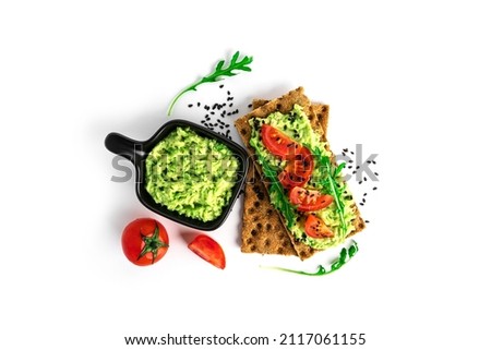Avocado sandwich with avocado cream and rye crisp bread for snack. Fiber, fitness and diet food. Rye bread with guacamole, arugula and cherry tomatoes isolated on a white background.  Royalty-Free Stock Photo #2117061155