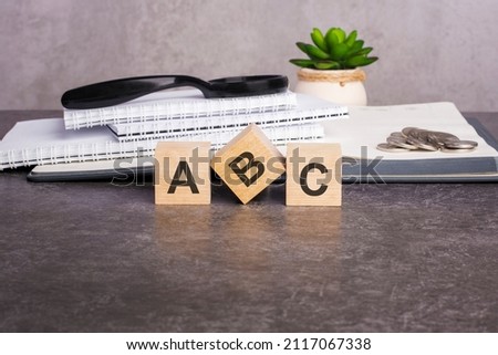 letters abc written on wooden cubes on a gray background. close-up of wooden elements. In the background is a green flower in a tub, stack of paper notebooks for writing and tablets