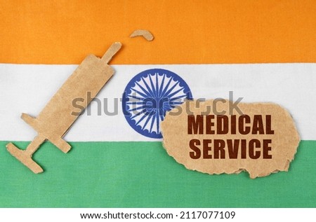 On the flag of India, a cardboard figure of a syringe and a torn cardboard with the inscription - MEDICAL SERVICE