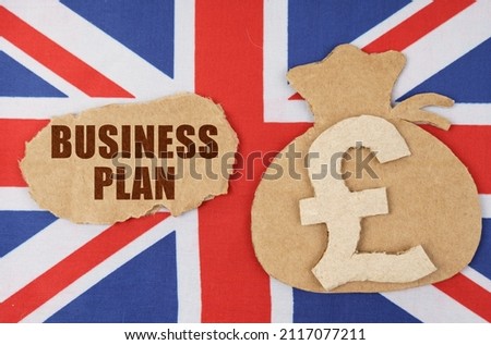 On the flag of Great Britain, a bag with a money symbol and a cardboard with the inscription - BUSINESS PLAN