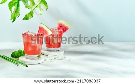 Fresh drink with watermelon and mint, cold summer lemonade, healthy mocktail. Sunny day shadows on blue sky background with copy space. Layout for wide banner. Royalty-Free Stock Photo #2117086037
