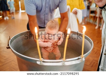 the baby boy is lowered into a font with holy water at baptism in the church. Orthodox Christian tradition. faith in God. family traditions.