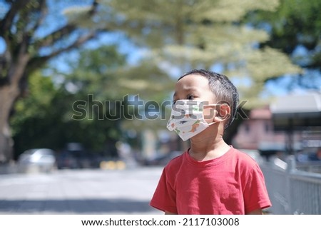 A young Asian kid wearing a face mask during the sunny day close up picture. 