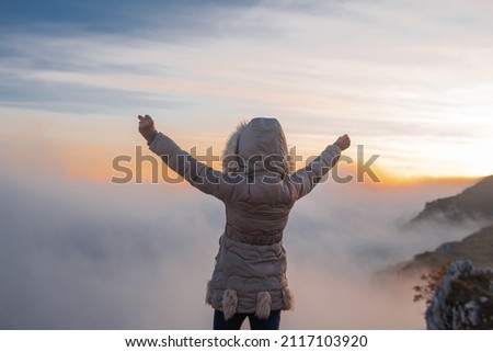 Happy girl with hands up on the top mountain at sunset. Concept of a people success freedom victory