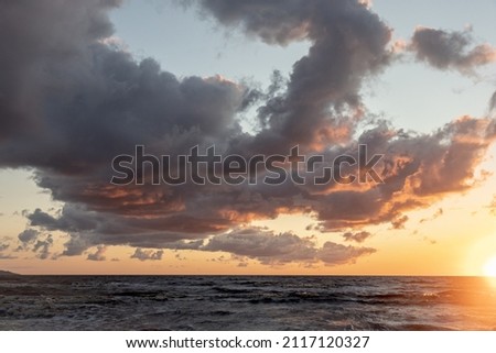 A scenic view of a seascape under cloudy sky at the sunset