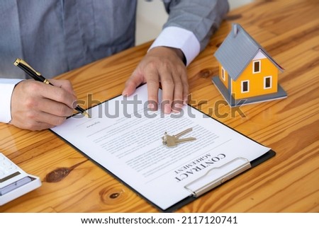 Real estate agent working sign agreement document contract for home loan insurance approving purchases for a client with house model and key on the table, concept of a contract to buy and sell a house