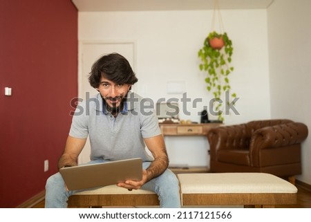 Young business man working at home from his living room chair with laptop on his lap. Home office concept. Gray notebook for working. Home office concept. High quality photo