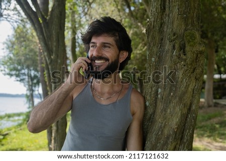 Young man at a park on a beautiful sunny day with mobile phone. Mobile phone for working and leisure. Home office concept. Green and nature background. High quality photo