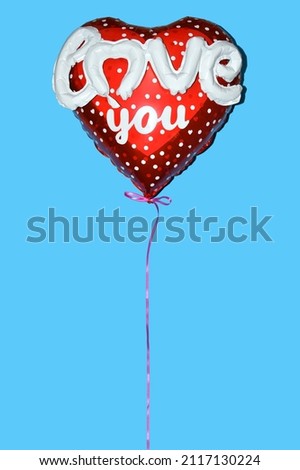 An inflated red foil heart-shaped balloon with the sign love you as a symbol of love and Valentine's Day on a blue background. Vertical.