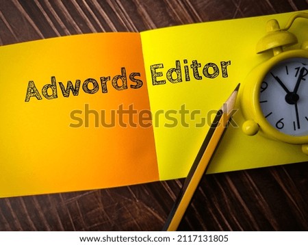 Top view pencil,clock and colored notepaper with text Adwords Editor on wooden background.