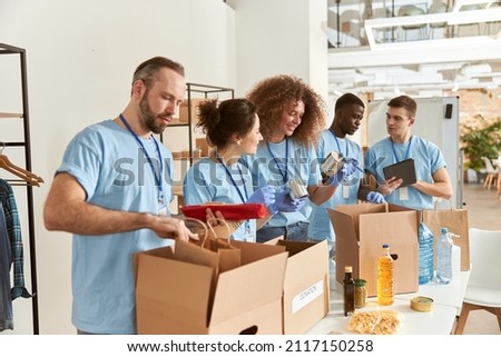 Team of diverse volunteers in protective gloves sorting, packing foodstuff in cardboard boxes, working together on donation project indoors Royalty-Free Stock Photo #2117150258