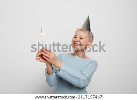 Woman wearing blue sweater and party hat, holding sparkles.