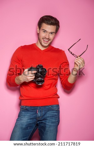 Portrait of young male with professional digital camera. man removed glasses standing over pink background. 