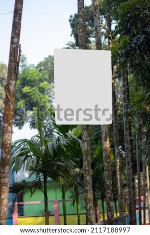 A blank white signboard hanging with a long tree and the background blur.