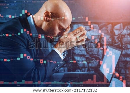 A male businessman is having a hard time falling stocks on the stock market while sitting in front of a laptop in the office. Pose of a tired or hard working person