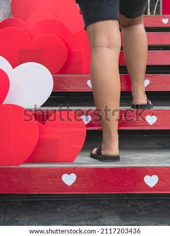 Young woman feet walking up stairs with beautiful red and white heart shape made from corrugated plastic sheets decorate on the stairs on the occasion of the Valentine's Day festival of love.