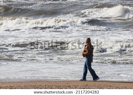 The woman walks along the beach and looks at the restless deep sea. Feeling calm, cool, relaxed.