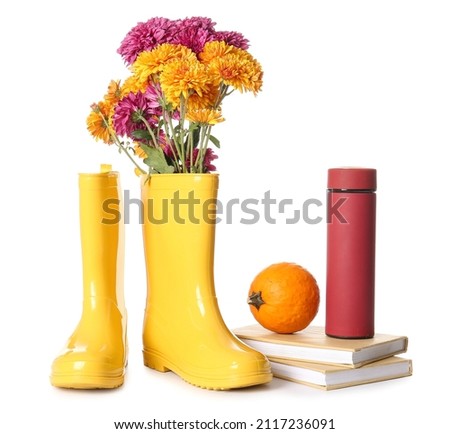 Rubber boots with flowers, thermos, books and pumpkin on white background
