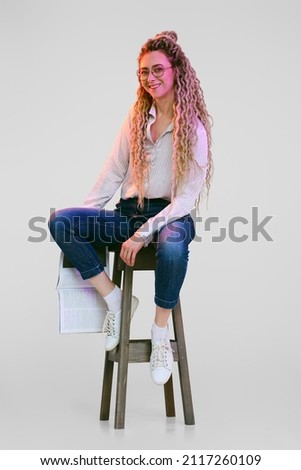 Woman with dreadlocks sits on tall chair and holds magazine in hand Royalty-Free Stock Photo #2117260109