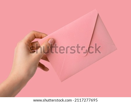 Woman hand receiving or giving pink envelope with love letter on pink background. Valentines day concept. High quality photo
