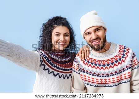 Happy young couple in warm sweaters taking selfie on color background