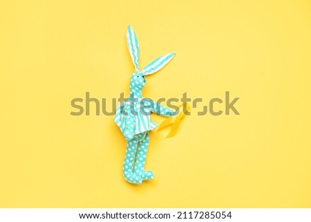 Toy rabbit with golden awareness ribbon on yellow background. International Childhood Cancer Day