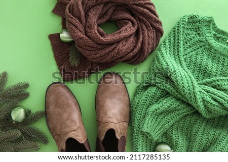 Knitted sweater, scarf, shoes and Christmas decor on green background, closeup