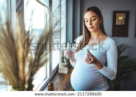 Picture of pregnant woman taking medication pills. Pregnant woman taking pill against heartburn. A young pregnant woman is taking medications and drinking water.