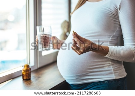 Pregnant woman reading label on bottle with medicine, with vitamins. Female sitting at home in bed with glass of water medicine. Pregnancy, health, pharmaceuticals, care and people. Royalty-Free Stock Photo #2117288603
