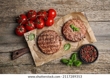 Tasty grilled hamburger patties with cherry tomatoes and seasonings on wooden table, flat lay Royalty-Free Stock Photo #2117289353