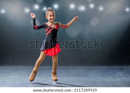 Little skater rides on rings in a red and black dress on the ice arena