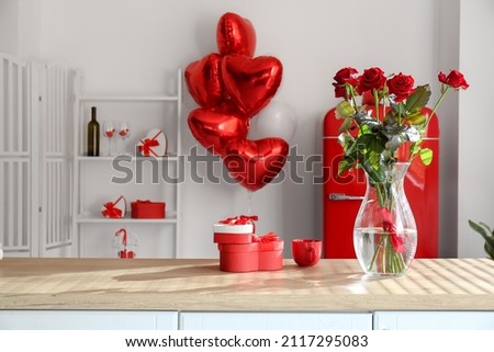 Vase with roses, cup and gift boxes on counter in room decorated for Valentine's Day celebration