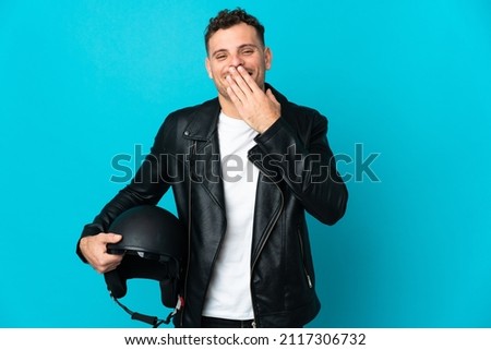 Caucasian man with a motorcycle helmet isolated on blue background happy and smiling covering mouth with hand