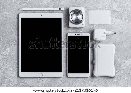 Top view of work space with white tablet, phone, camera and portable hard drive on grey concrete background
